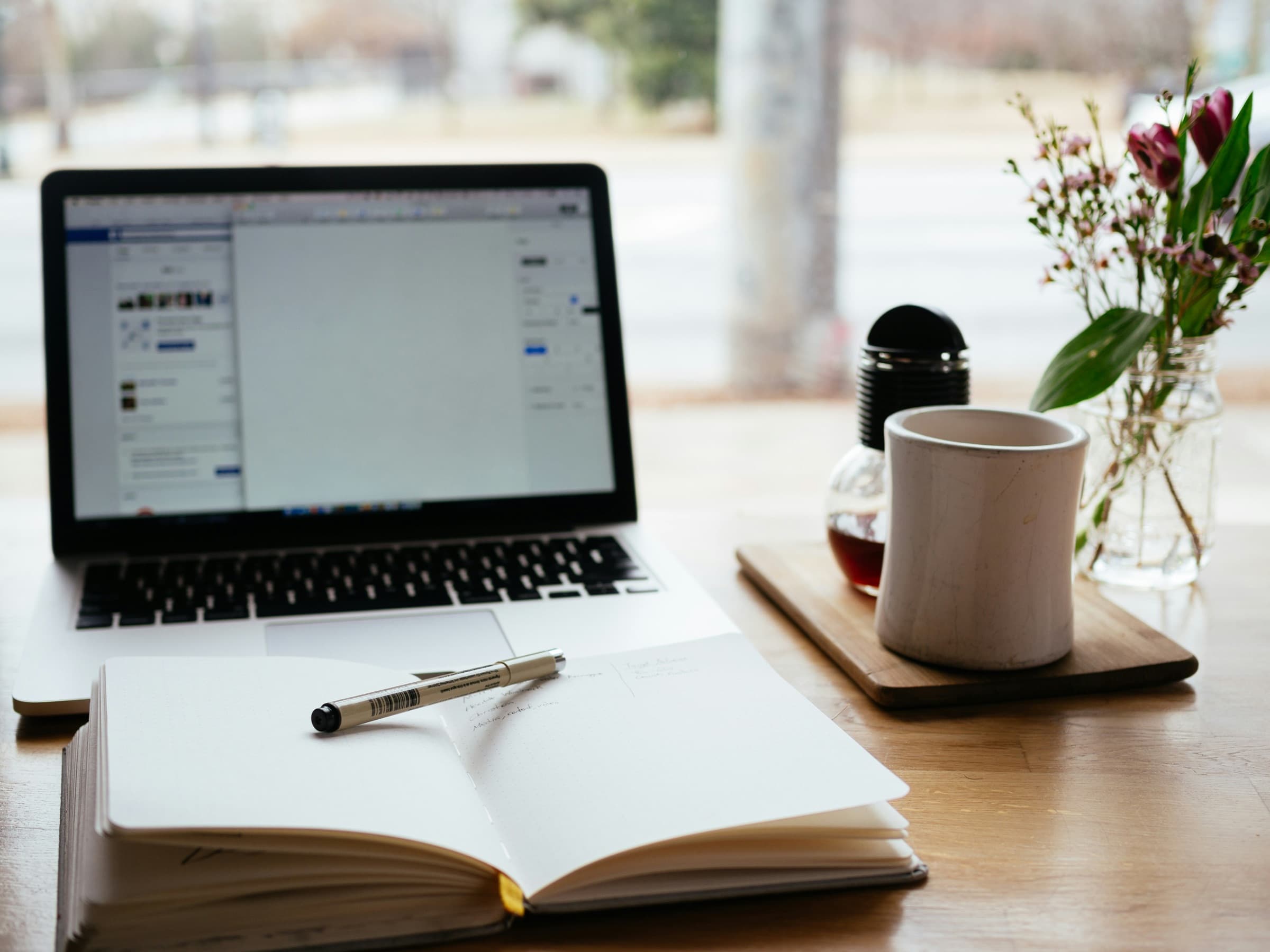 A tidy workspace with a laptop, notebook and coffee